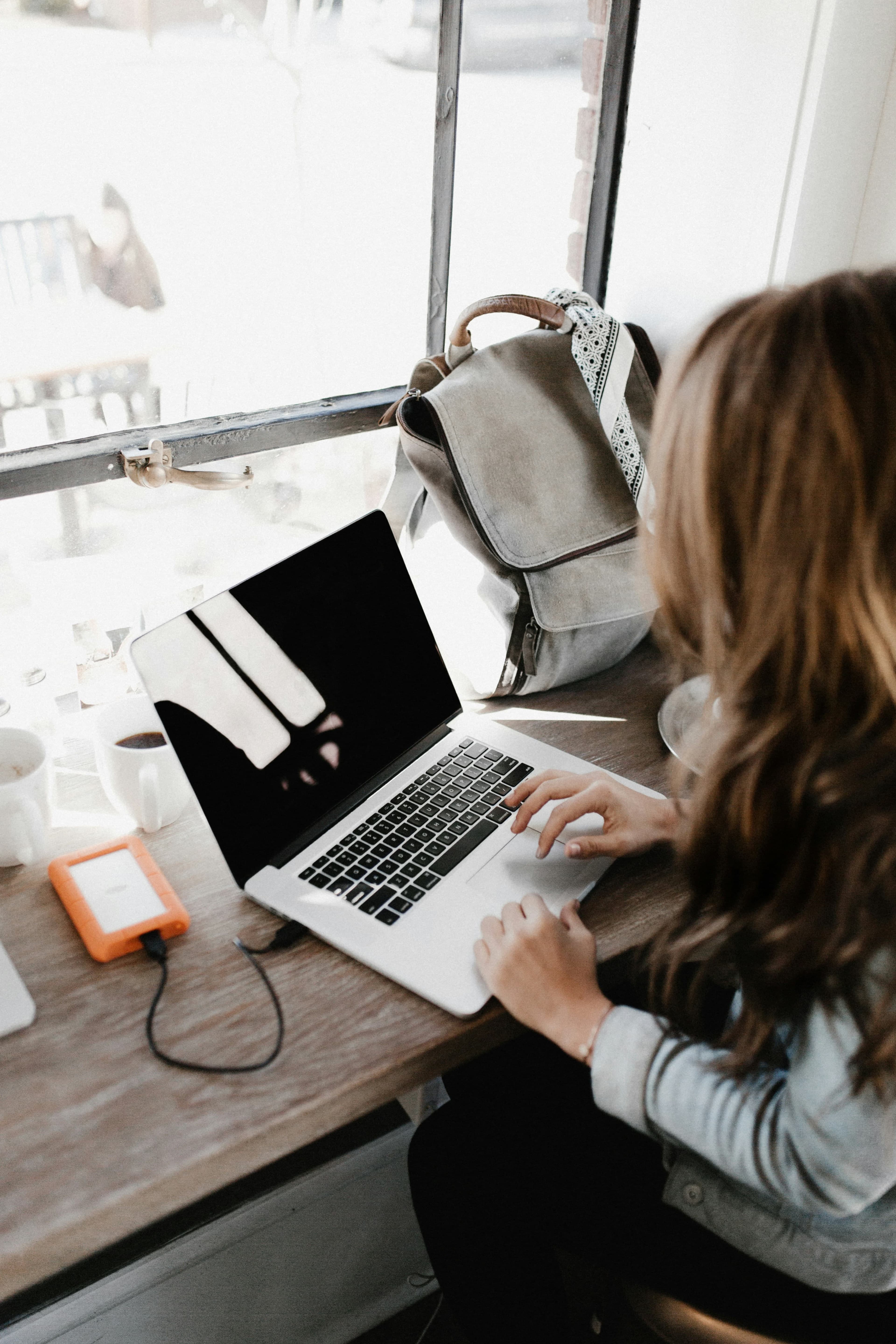 Girl wearing grey long-sleeved shirt using MacBook Pro on brown wooden table